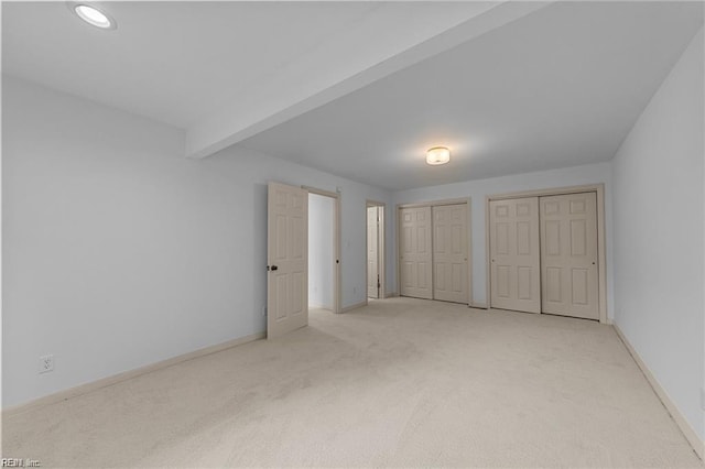 unfurnished bedroom with beamed ceiling, two closets, baseboards, and carpet floors