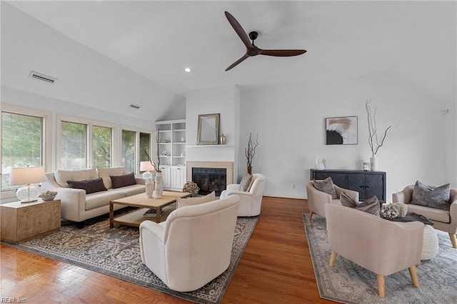 living area featuring visible vents, built in shelves, wood finished floors, a glass covered fireplace, and vaulted ceiling