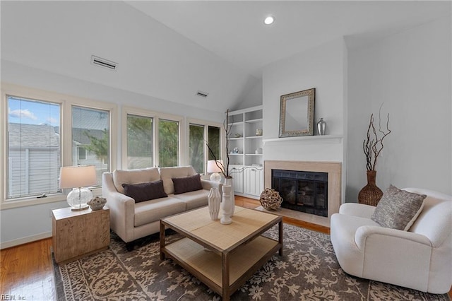 living area featuring visible vents, a fireplace with flush hearth, built in features, wood finished floors, and lofted ceiling