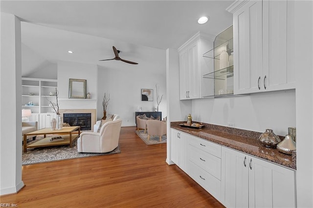 living area featuring built in features, a ceiling fan, light wood finished floors, recessed lighting, and a glass covered fireplace