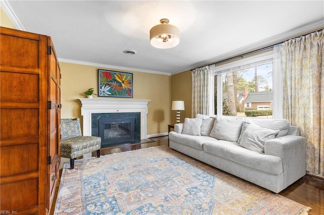 living room featuring a glass covered fireplace, crown molding, visible vents, and wood finished floors