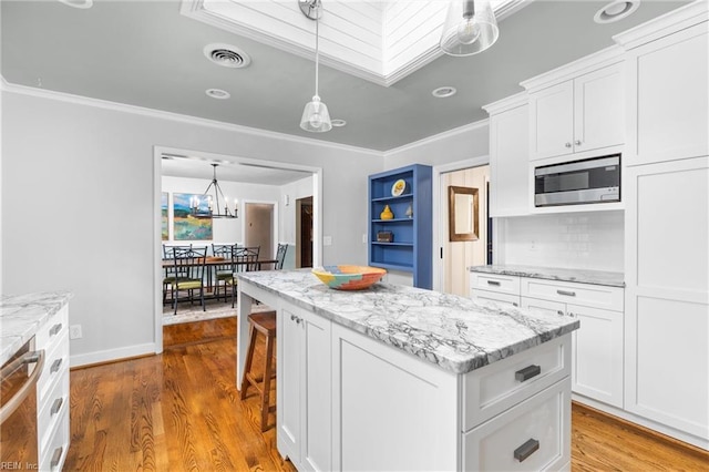 kitchen featuring visible vents, a kitchen island, ornamental molding, white cabinetry, and stainless steel microwave