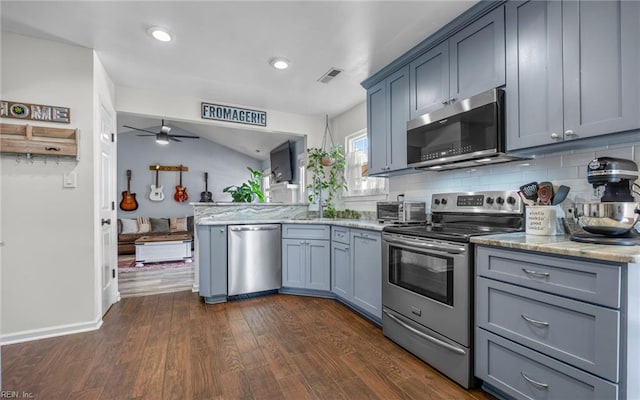 kitchen featuring visible vents, light stone counters, a peninsula, stainless steel appliances, and dark wood-style flooring