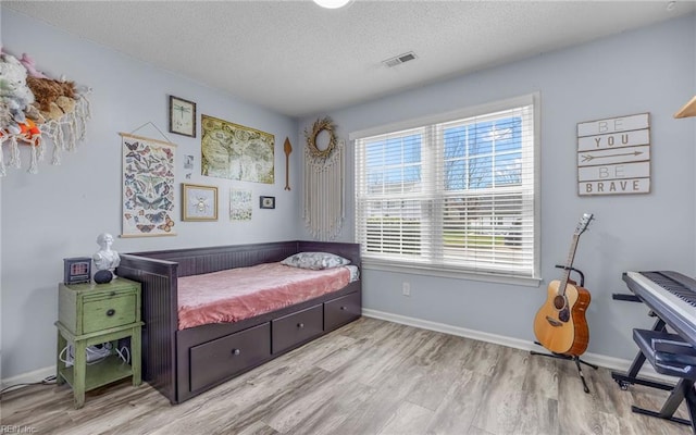 bedroom with visible vents, baseboards, a textured ceiling, and wood finished floors