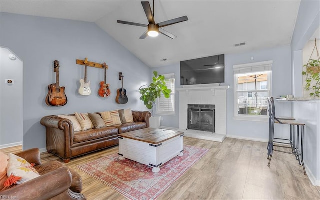 living area with visible vents, a brick fireplace, ceiling fan, lofted ceiling, and light wood-style floors