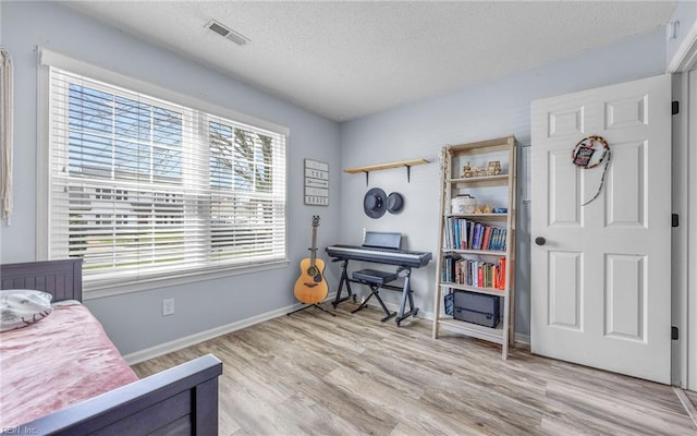 bedroom featuring baseboards, wood finished floors, visible vents, and a textured ceiling