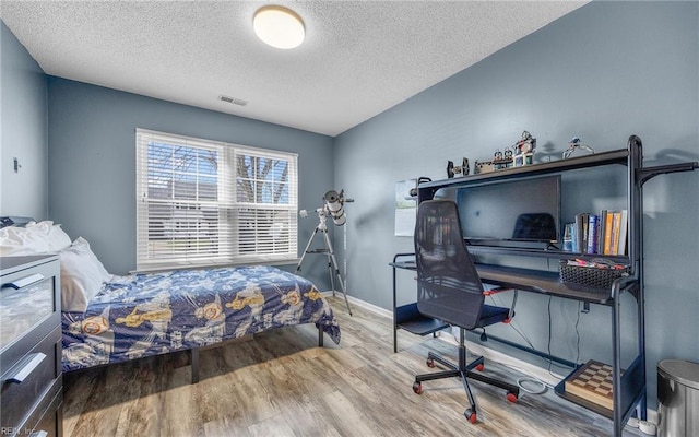 bedroom with baseboards, wood finished floors, visible vents, and a textured ceiling