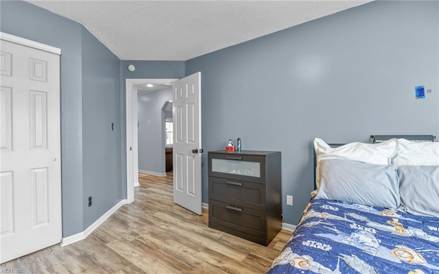 bedroom with a textured ceiling, baseboards, and wood finished floors