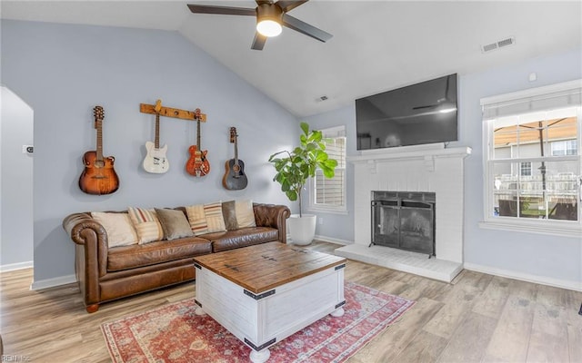 living area featuring visible vents, lofted ceiling, a brick fireplace, and light wood-style flooring