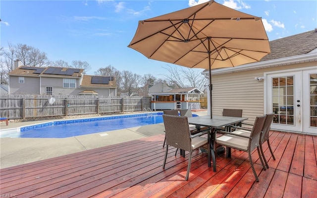 view of swimming pool featuring outdoor dining area, a fenced backyard, french doors, a wooden deck, and a fenced in pool