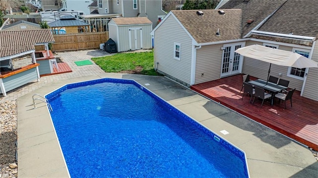 view of swimming pool with a shed, a wooden deck, a fenced backyard, an outdoor structure, and french doors