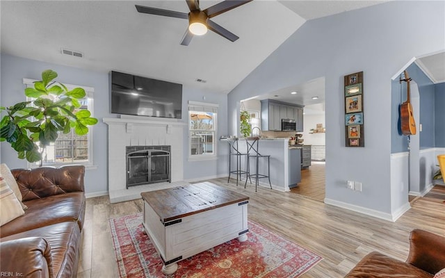 living room with visible vents, ceiling fan, a brick fireplace, and light wood-style floors