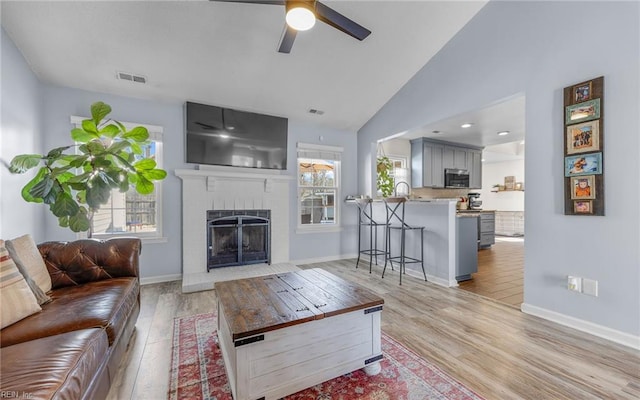 living room featuring visible vents, light wood-style floors, a fireplace, and vaulted ceiling