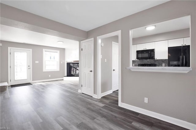 interior space with decorative backsplash, white cabinets, black appliances, and baseboards