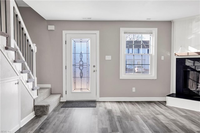 foyer entrance with visible vents, wood finished floors, a fireplace, baseboards, and stairs