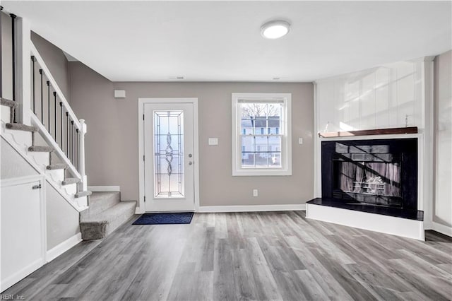 entryway featuring baseboards, a large fireplace, wood finished floors, and stairs