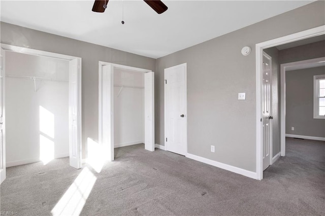 unfurnished bedroom featuring baseboards, two closets, a ceiling fan, and carpet