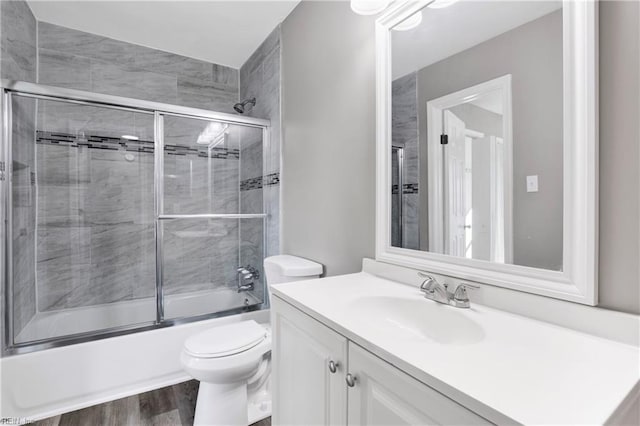 full bathroom featuring toilet, wood finished floors, vanity, and bath / shower combo with glass door