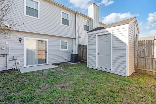 rear view of property featuring fence, a shed, central air condition unit, a yard, and an outbuilding