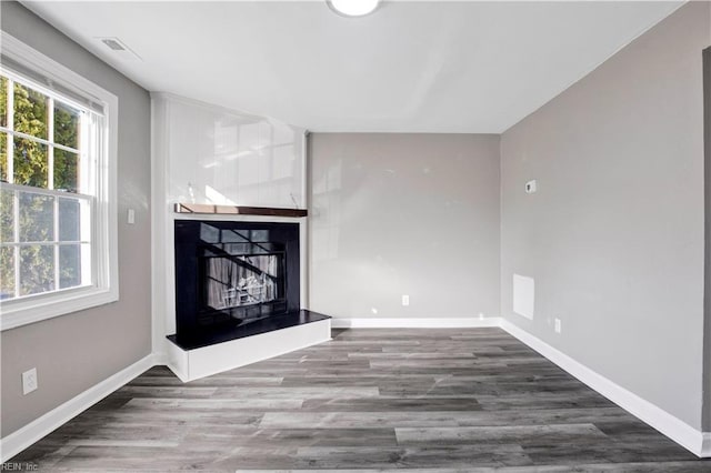 unfurnished living room with visible vents, a fireplace with raised hearth, baseboards, and wood finished floors