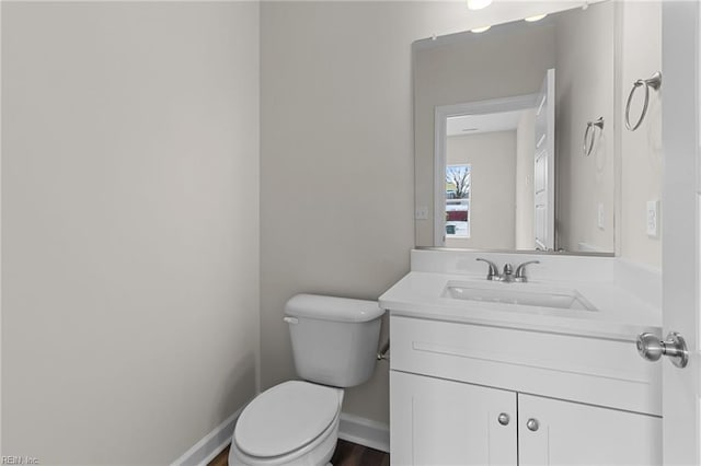 half bathroom featuring vanity, toilet, and baseboards