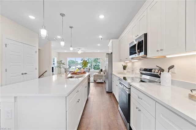 kitchen with light countertops, appliances with stainless steel finishes, wood finished floors, white cabinetry, and a sink