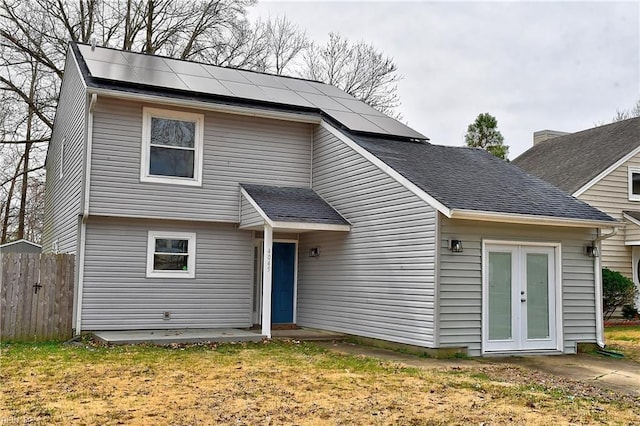 view of front facade featuring french doors, roof mounted solar panels, roof with shingles, and fence