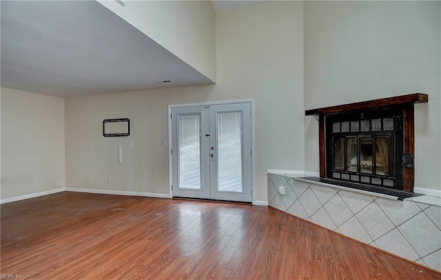 unfurnished living room with french doors, wood finished floors, baseboards, and a fireplace with raised hearth