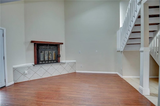 unfurnished living room with a towering ceiling, a multi sided fireplace, wood finished floors, and stairs