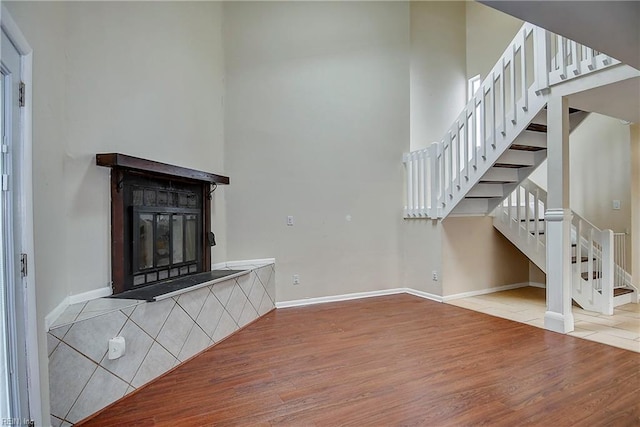 unfurnished living room with wood finished floors, baseboards, a high ceiling, stairs, and a glass covered fireplace