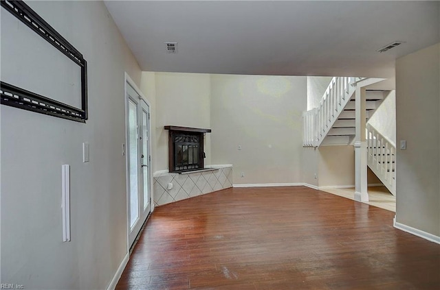 unfurnished living room with baseboards, wood finished floors, visible vents, and a fireplace with raised hearth