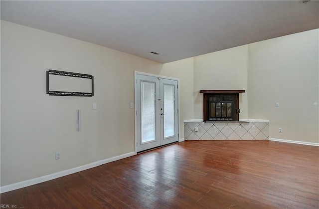 unfurnished living room featuring visible vents, baseboards, french doors, wood finished floors, and a glass covered fireplace