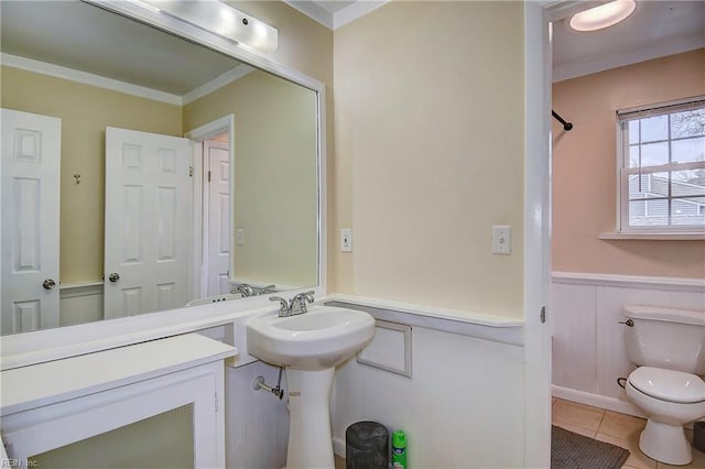 bathroom with a wainscoted wall, a sink, tile patterned flooring, crown molding, and toilet