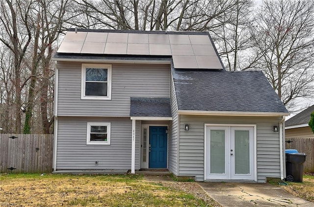 view of front of property featuring solar panels, fence, and a shingled roof