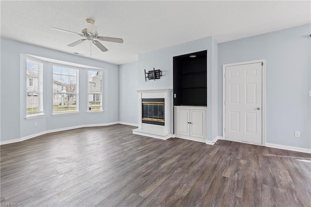 unfurnished living room featuring ceiling fan, baseboards, a glass covered fireplace, and dark wood finished floors