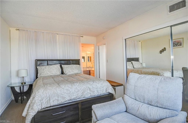 carpeted bedroom featuring baseboards, visible vents, ensuite bath, a closet, and a textured ceiling