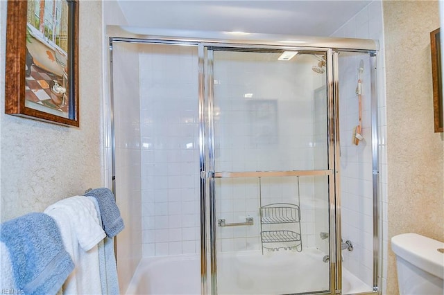 full bath with enclosed tub / shower combo, toilet, and a textured wall