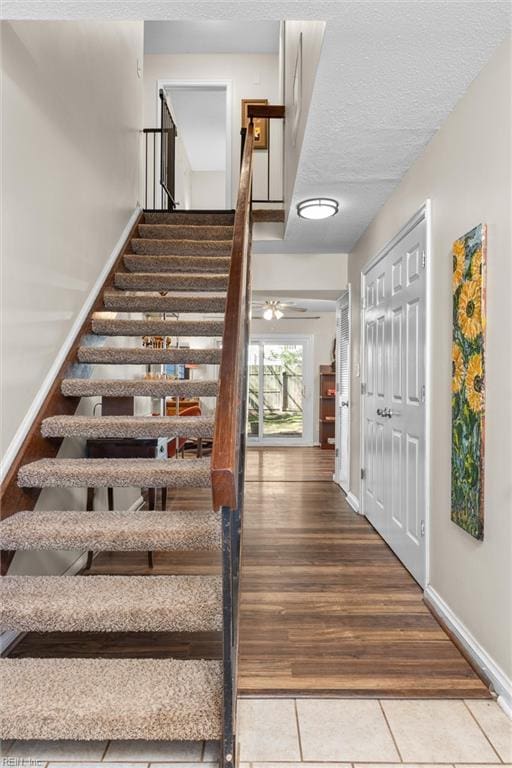 staircase with tile patterned floors, a textured ceiling, and baseboards