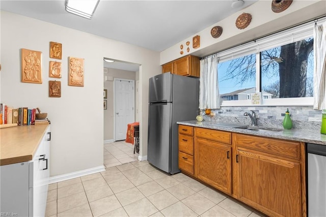 kitchen featuring a sink, backsplash, stainless steel appliances, brown cabinetry, and light tile patterned floors