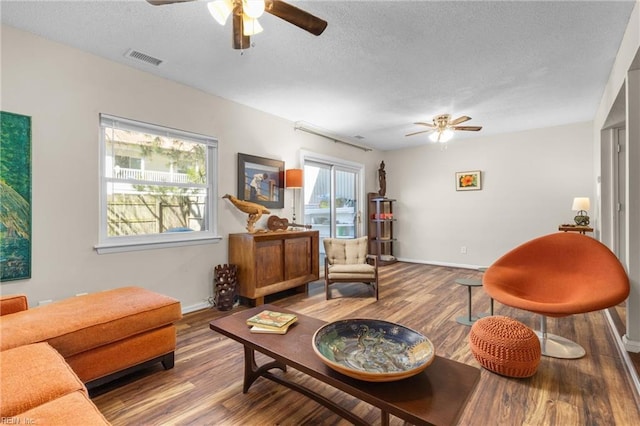 living room with visible vents, a textured ceiling, baseboards, and wood finished floors