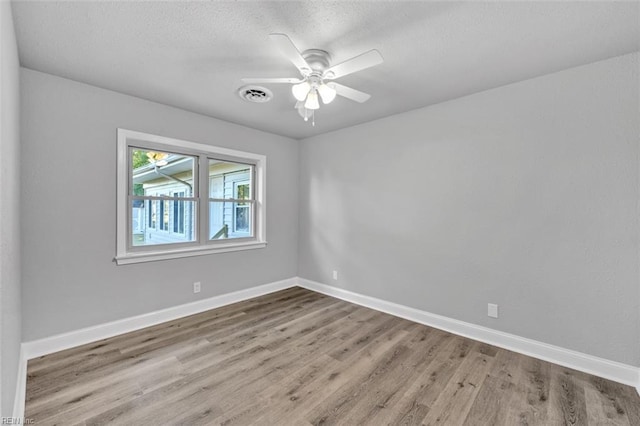 spare room featuring a ceiling fan, wood finished floors, baseboards, visible vents, and a textured ceiling