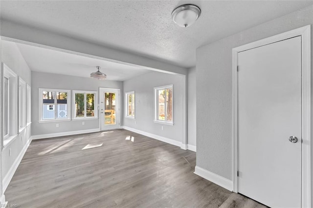 unfurnished living room with wood finished floors, baseboards, a textured wall, and a textured ceiling