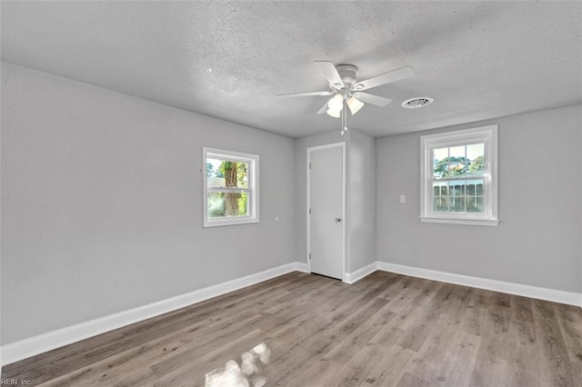 unfurnished bedroom featuring visible vents, a textured ceiling, wood finished floors, baseboards, and ceiling fan