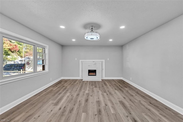 unfurnished living room with wood finished floors, baseboards, a warm lit fireplace, and a textured ceiling
