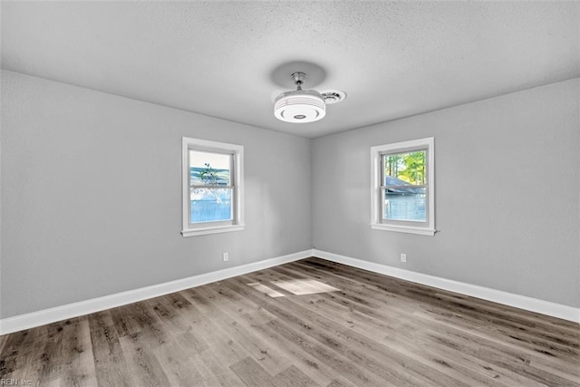 spare room featuring a wealth of natural light, baseboards, a textured ceiling, and wood finished floors