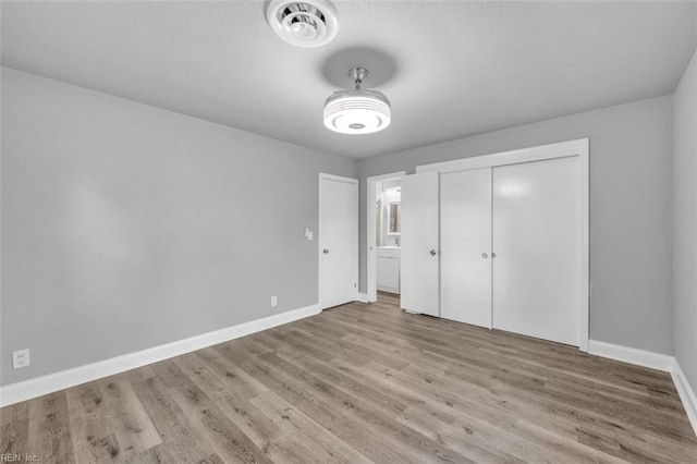 unfurnished bedroom featuring visible vents, a textured ceiling, baseboards, and wood finished floors