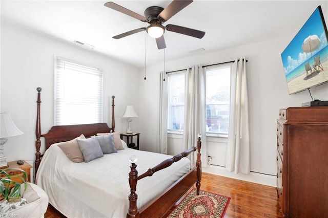 bedroom featuring ceiling fan, visible vents, multiple windows, and wood finished floors