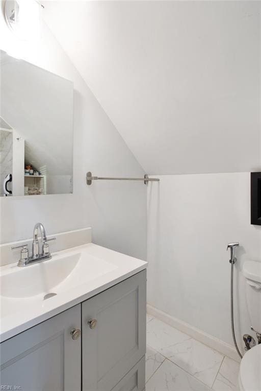 bathroom with baseboards, toilet, lofted ceiling, marble finish floor, and vanity