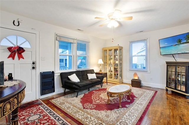 living room with hardwood / wood-style floors, heating unit, visible vents, baseboards, and ceiling fan