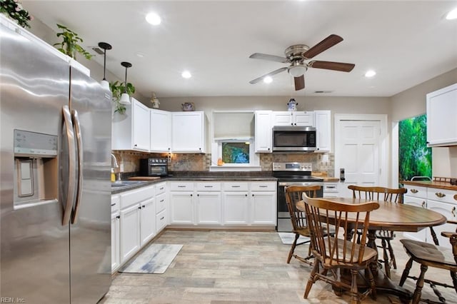 kitchen with a sink, white cabinets, appliances with stainless steel finishes, dark countertops, and tasteful backsplash